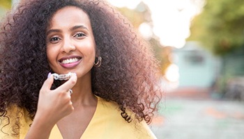 Woman standing outside, holding clear orthodontic aligner