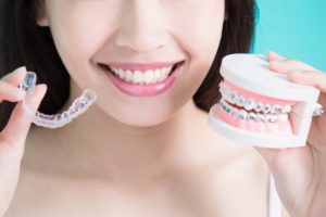 Woman holding clear aligner and braces