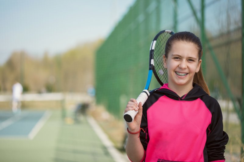 a young girl with braces playing tennis