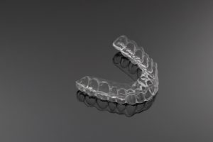 Clear Invisalign retainer isolated against dark gray background