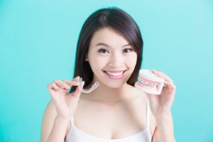 Woman holding Invisalign aligner and dental model with braces