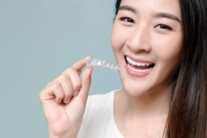 Happy woman with dental restorations holding Invisalign aligner