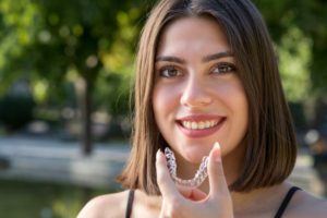 Smiling woman holding Invisalign aligner close to her mouth