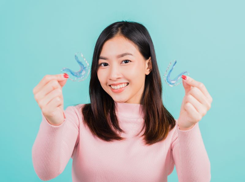 Smiling woman holding two orthodontic retainers