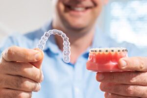 Man holding model with braces and Invisalign aligner